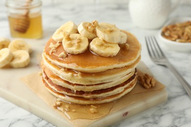 Photo of Delicious pancakes with bananas, walnuts and honey on white marble table, closeup