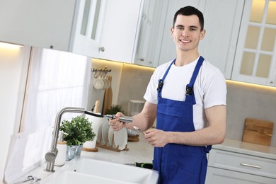Photo of Smiling plumber repairing faucet with spanner in kitchen