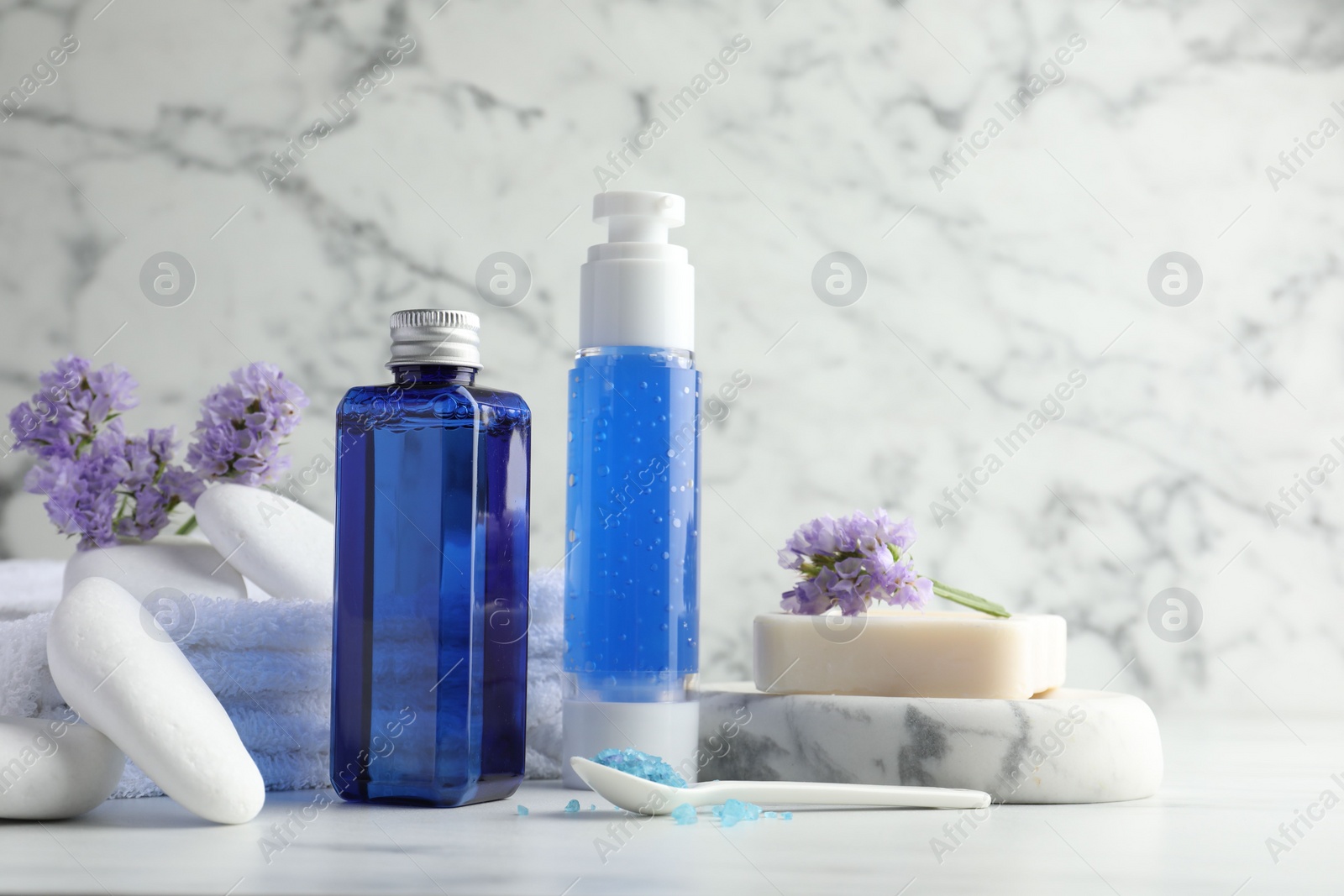 Photo of Spa composition. Bottles of cosmetic products, sea salt, stones, soap and flowers on white marble table