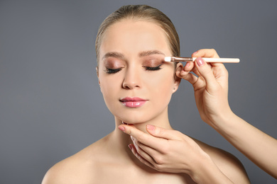 Artist applying makeup onto woman's face on light grey background