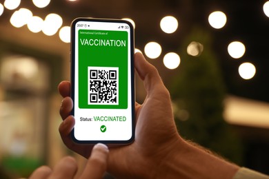Man holding smartphone with international certificate of vaccination outdoors, closeup