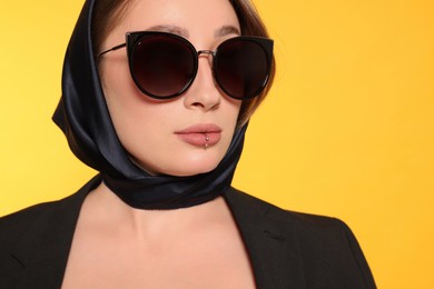 Photo of Young woman with lip piercing and sunglasses on yellow background