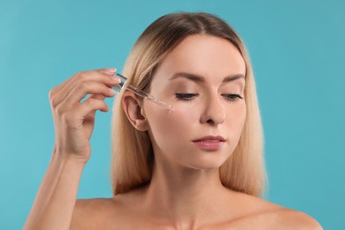 Photo of Beautiful woman applying cosmetic serum onto her face on light blue background