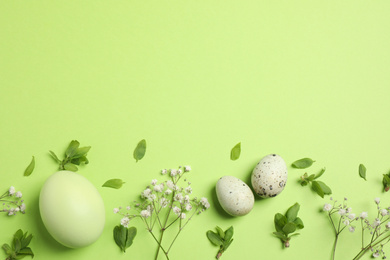 Beautiful flat lay composition with flowers and Easter eggs on green background. Space for text