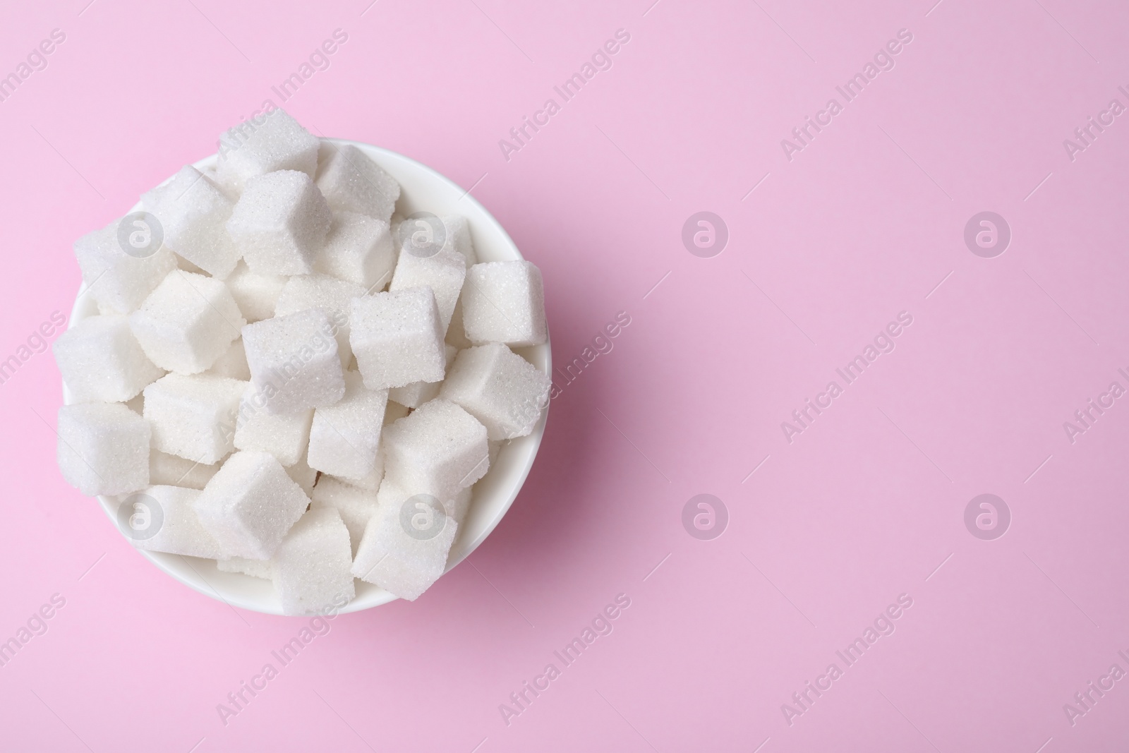 Photo of Refined sugar cubes in bowl on pink background, top view. Space for text