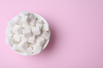 Refined sugar cubes in bowl on pink background, top view. Space for text