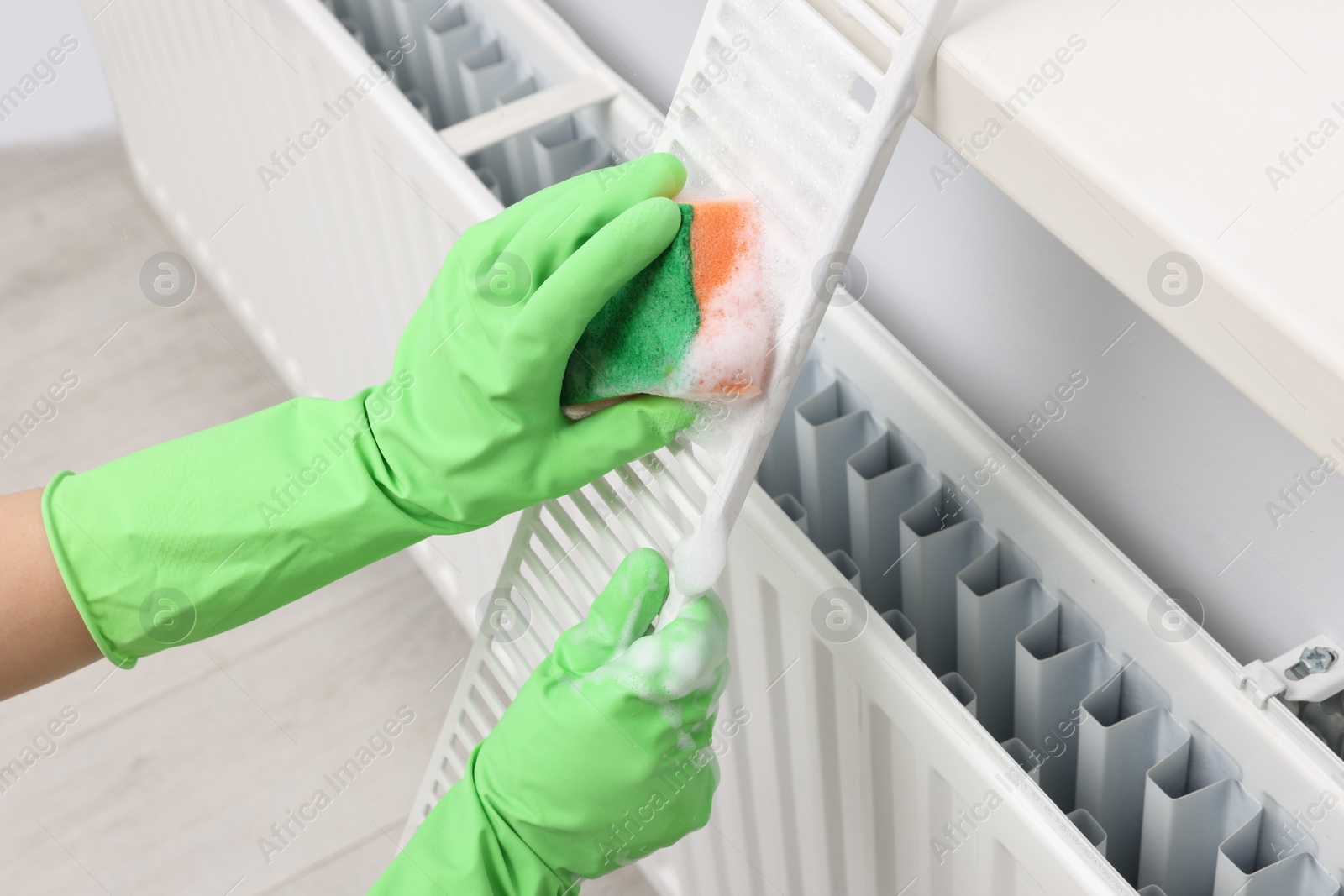 Photo of Woman washing radiator grill with sponge and detergent indoors, closeup