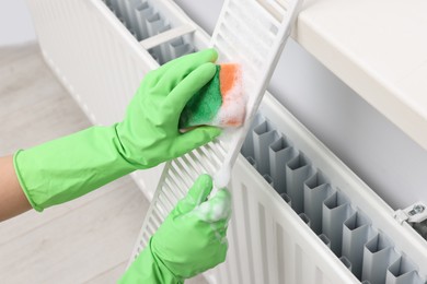 Woman washing radiator grill with sponge and detergent indoors, closeup