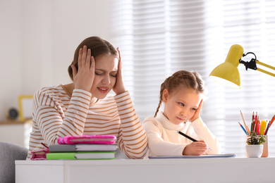 Photo of Upset mother and daughter doing homework together at table indoors