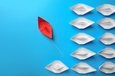 Photo of Red paper boat floating away from others on light blue background, flat lay with space for text. Uniqueness concept