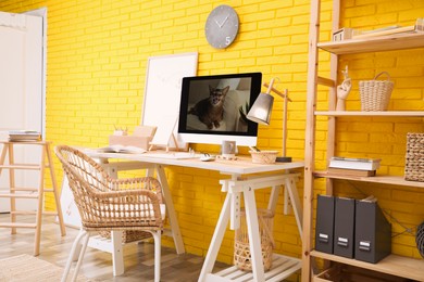 Stylish home office interior with comfortable workplace near yellow brick wall