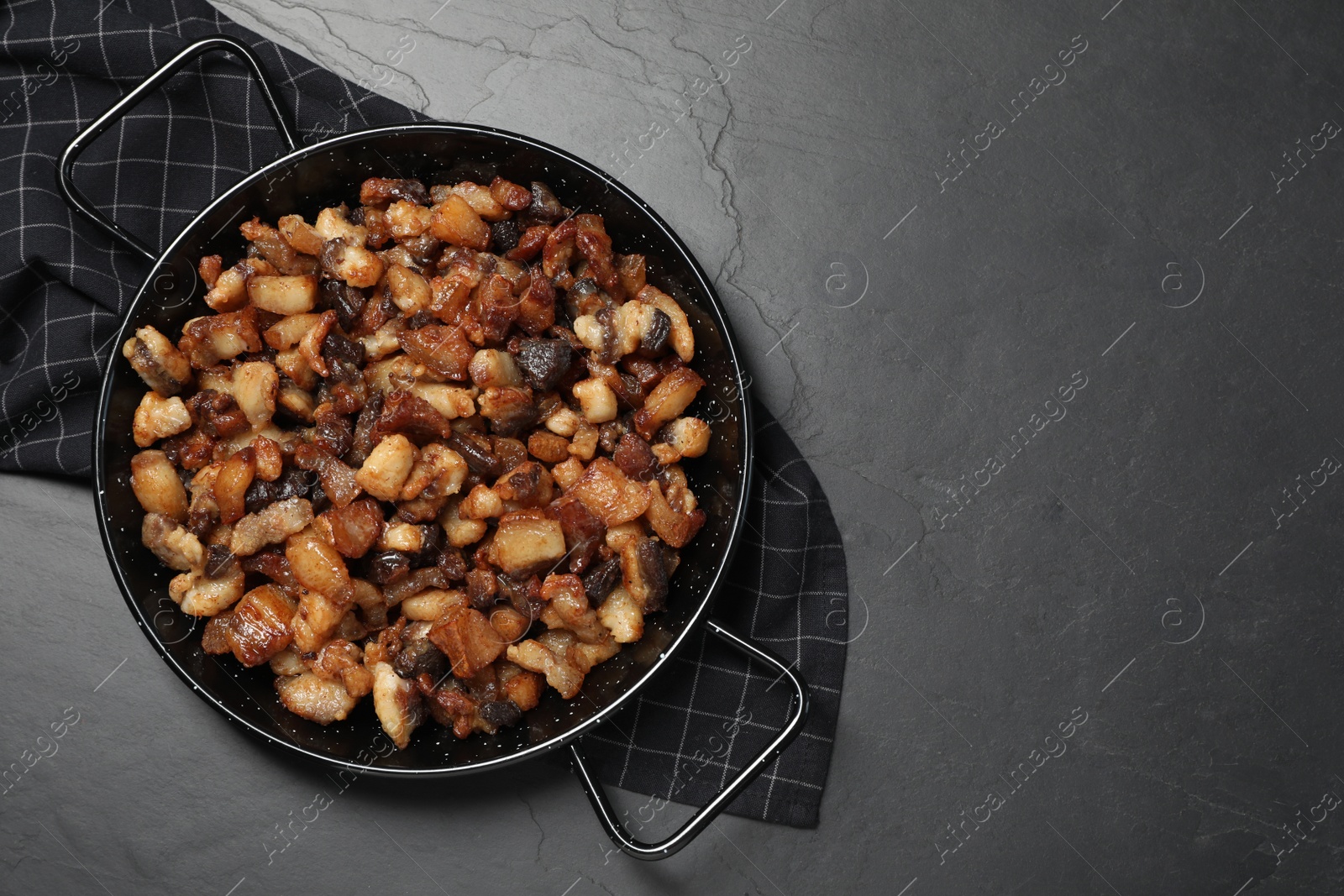 Photo of Tasty fried cracklings on black table, top view with space for text. Cooked pork lard