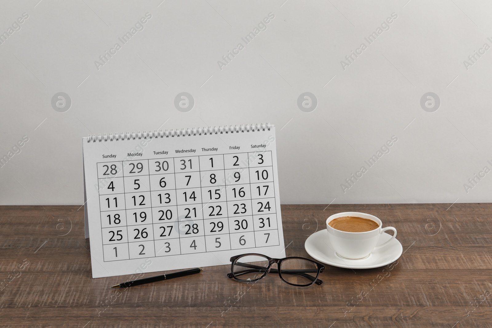 Photo of Calendar, glasses and cup of coffee on wooden table