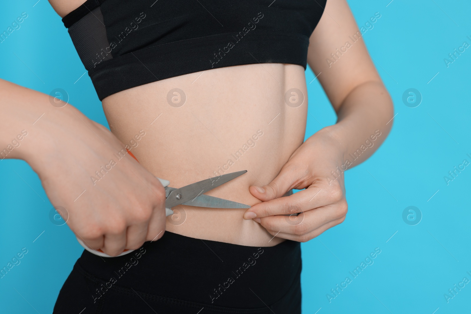 Photo of Slim woman with scissors on light blue background, closeup. Weight loss surgery