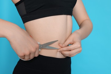 Slim woman with scissors on light blue background, closeup. Weight loss surgery