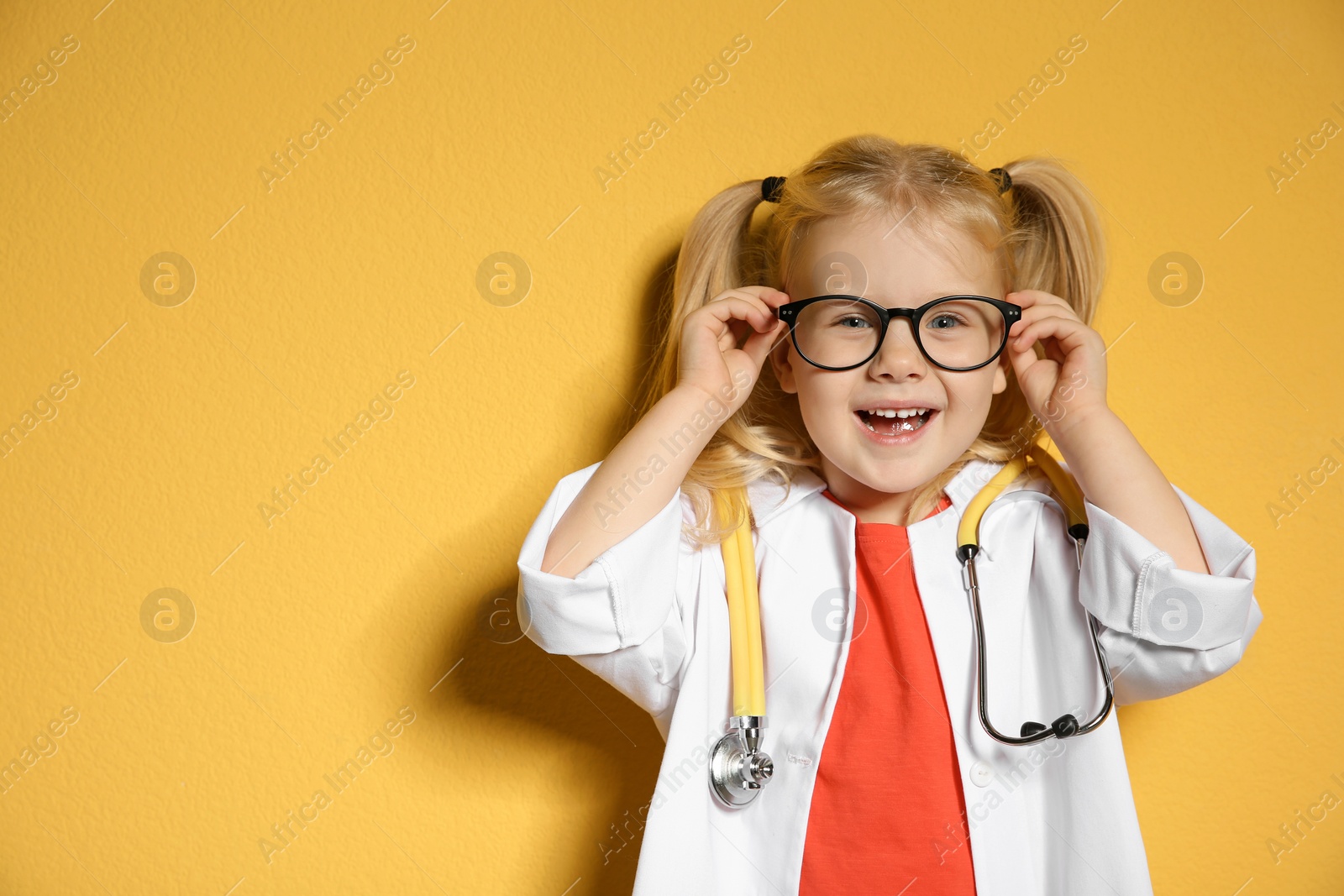 Photo of Cute child in doctor coat with stethoscope on color background. Space for text
