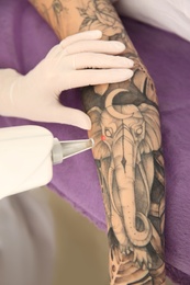Photo of Young woman undergoing laser tattoo removal procedure in salon, closeup