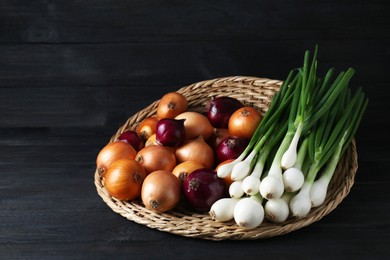 Photo of Wicker mat with different kinds of onions on black wooden table