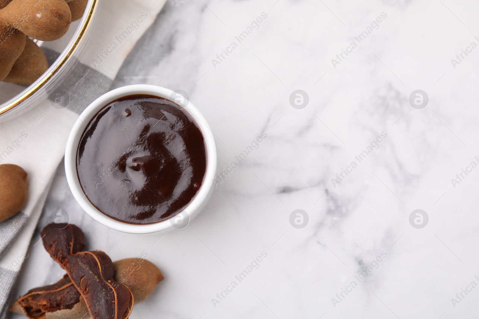 Bowl of tamarind sauce and fresh pods on white marble table, flat lay. Space for text Photo of Bowl of tamarind sauce and fresh pods on white marble table, flat lay. Space for text