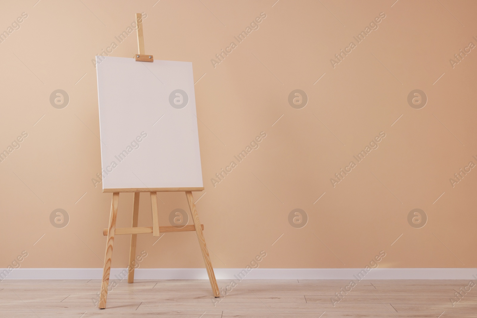 Photo of Wooden easel with blank canvas near beige wall indoors. Space for text