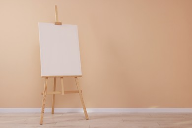 Photo of Wooden easel with blank canvas near beige wall indoors. Space for text