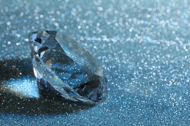 Beautiful dazzling diamond on blue glitter background, closeup. Space for text
