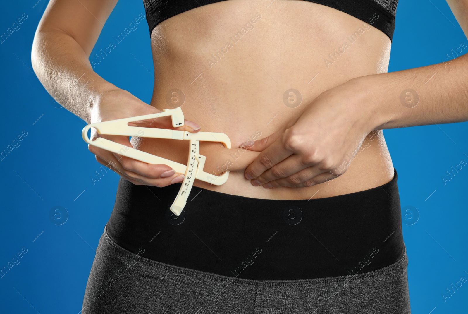 Photo of Young woman measuring body fat with caliper on blue background, closeup