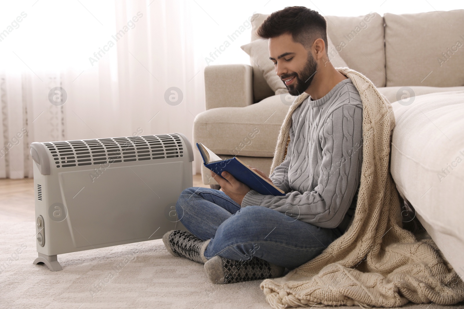 Photo of Young man warming up near electric heater at home