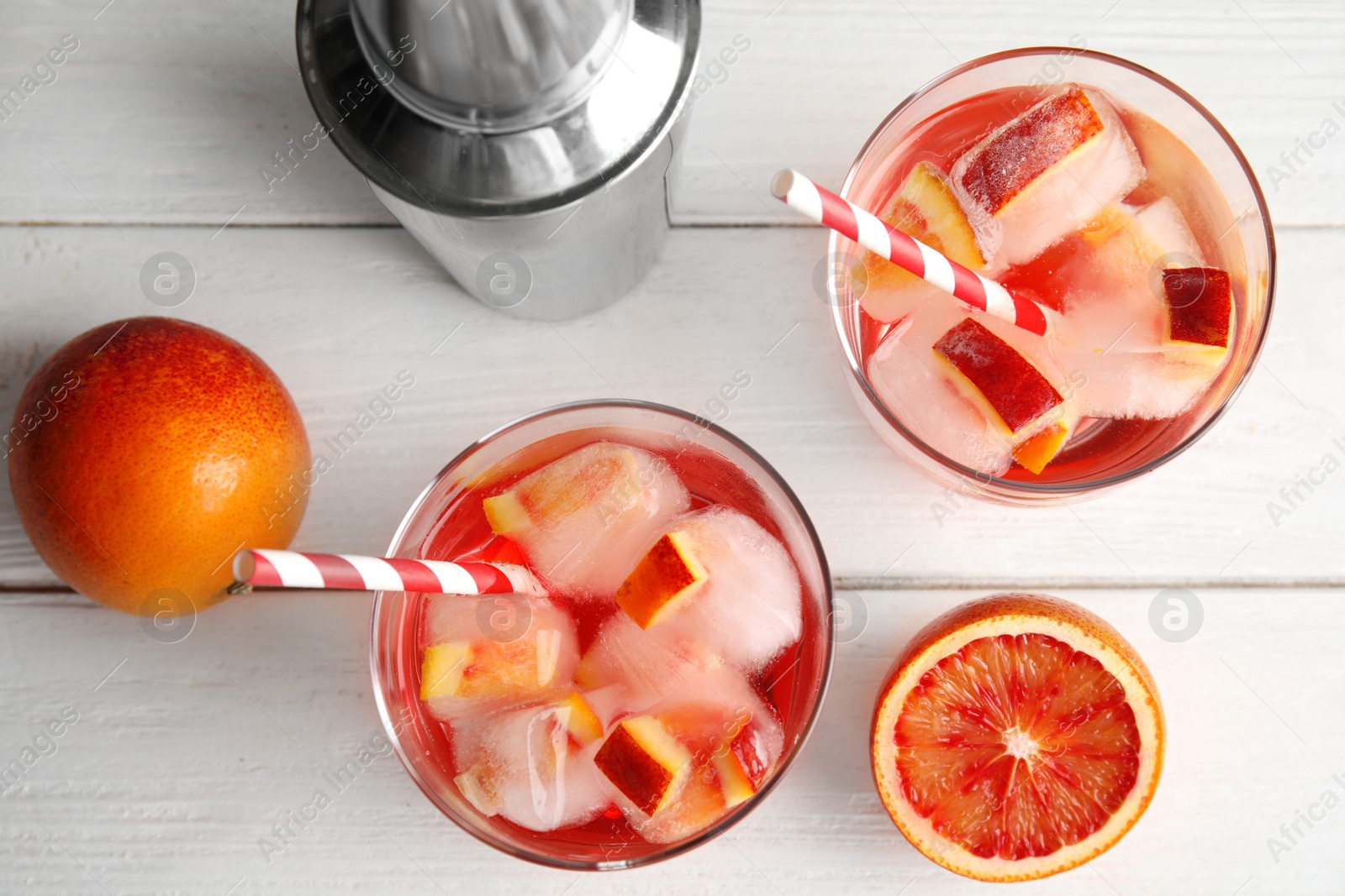 Photo of Tropical cocktail with ice cubes in glasses, fruit and shaker on wooden background, flat lay