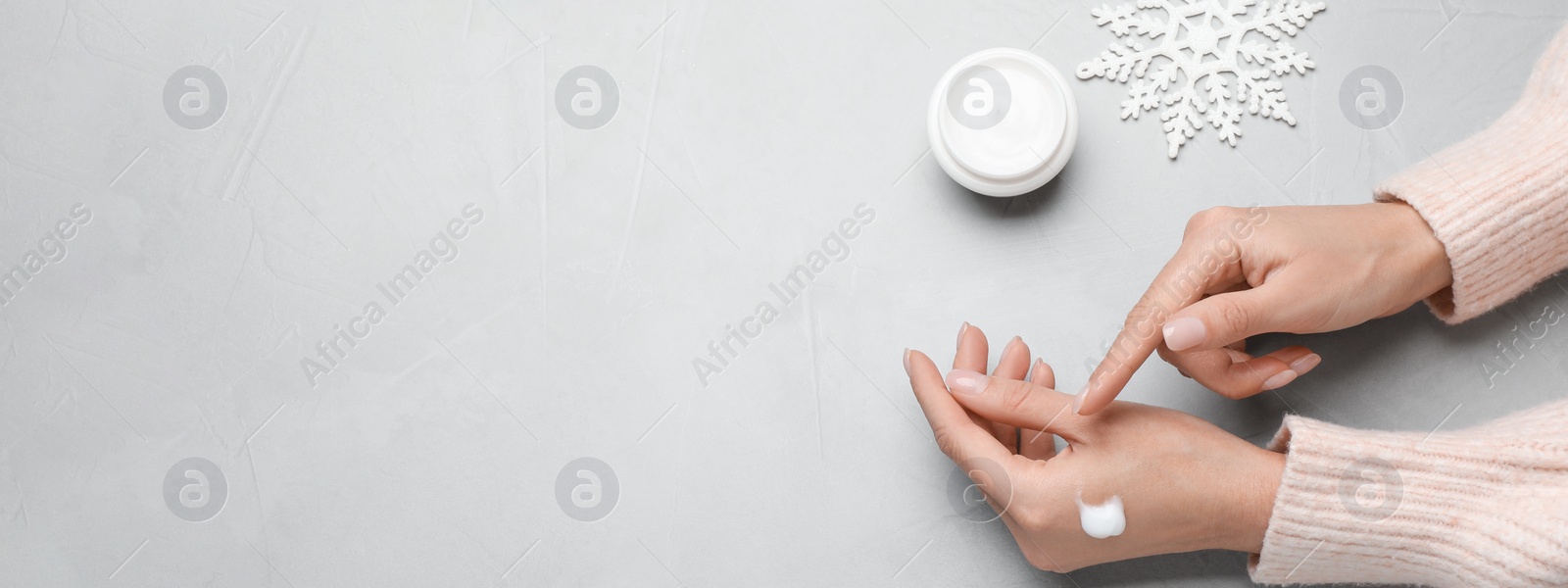 Image of Woman applying cream onto hand on light grey table, top view with space for text. Banner design