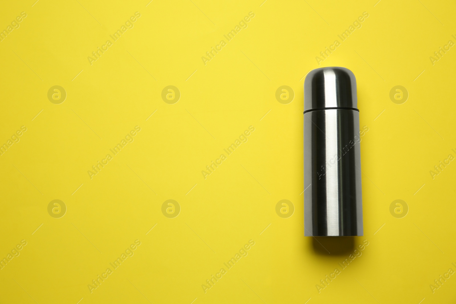 Photo of Stainless steel thermos on yellow background, top view. Space for text