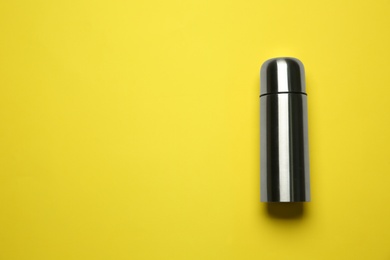 Photo of Stainless steel thermos on yellow background, top view. Space for text