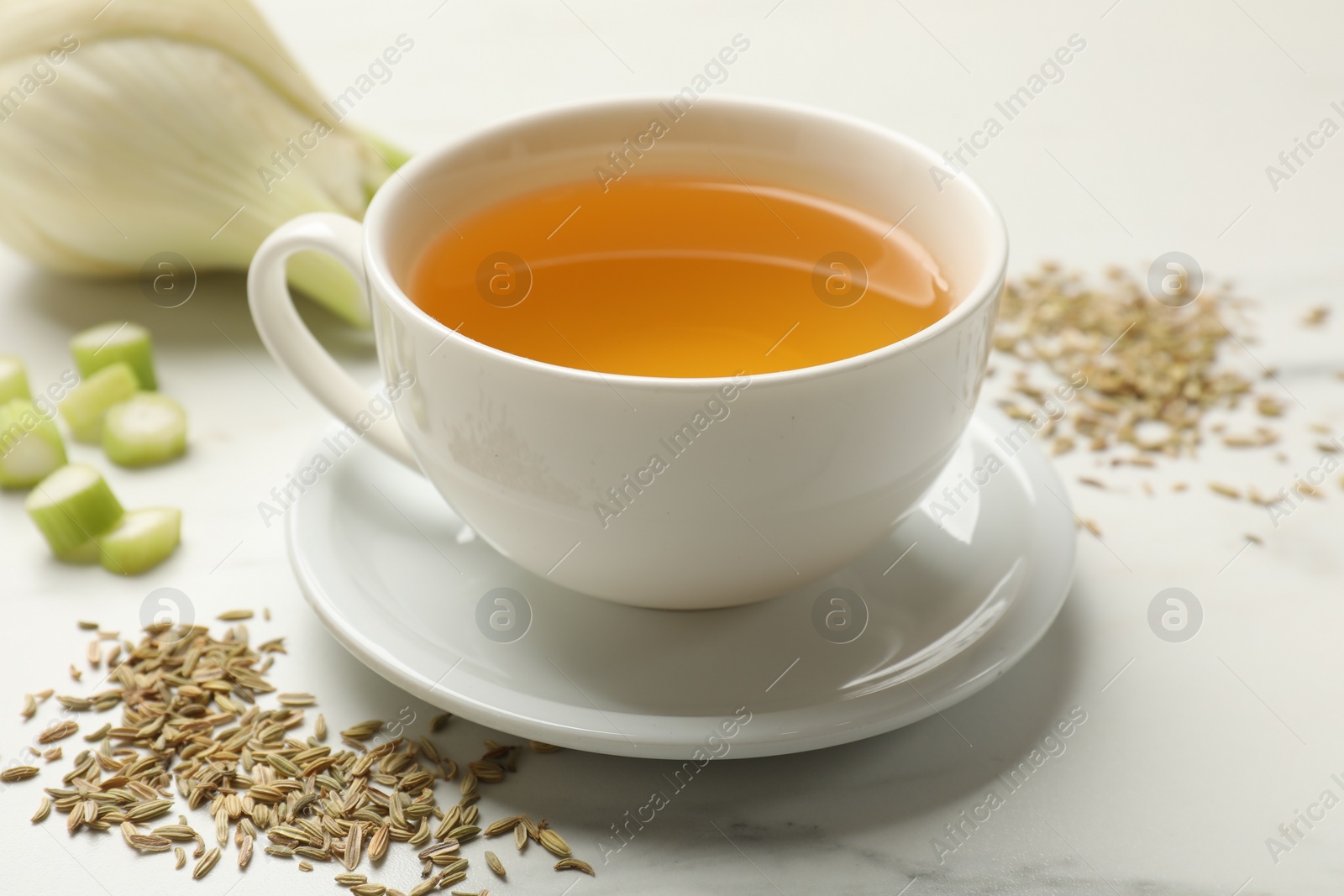 Photo of Fennel tea in cup, seeds and fresh vegetable on white marble table, closeup