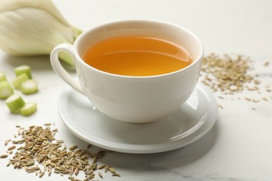 Photo of Fennel tea in cup, seeds and fresh vegetable on white marble table, closeup
