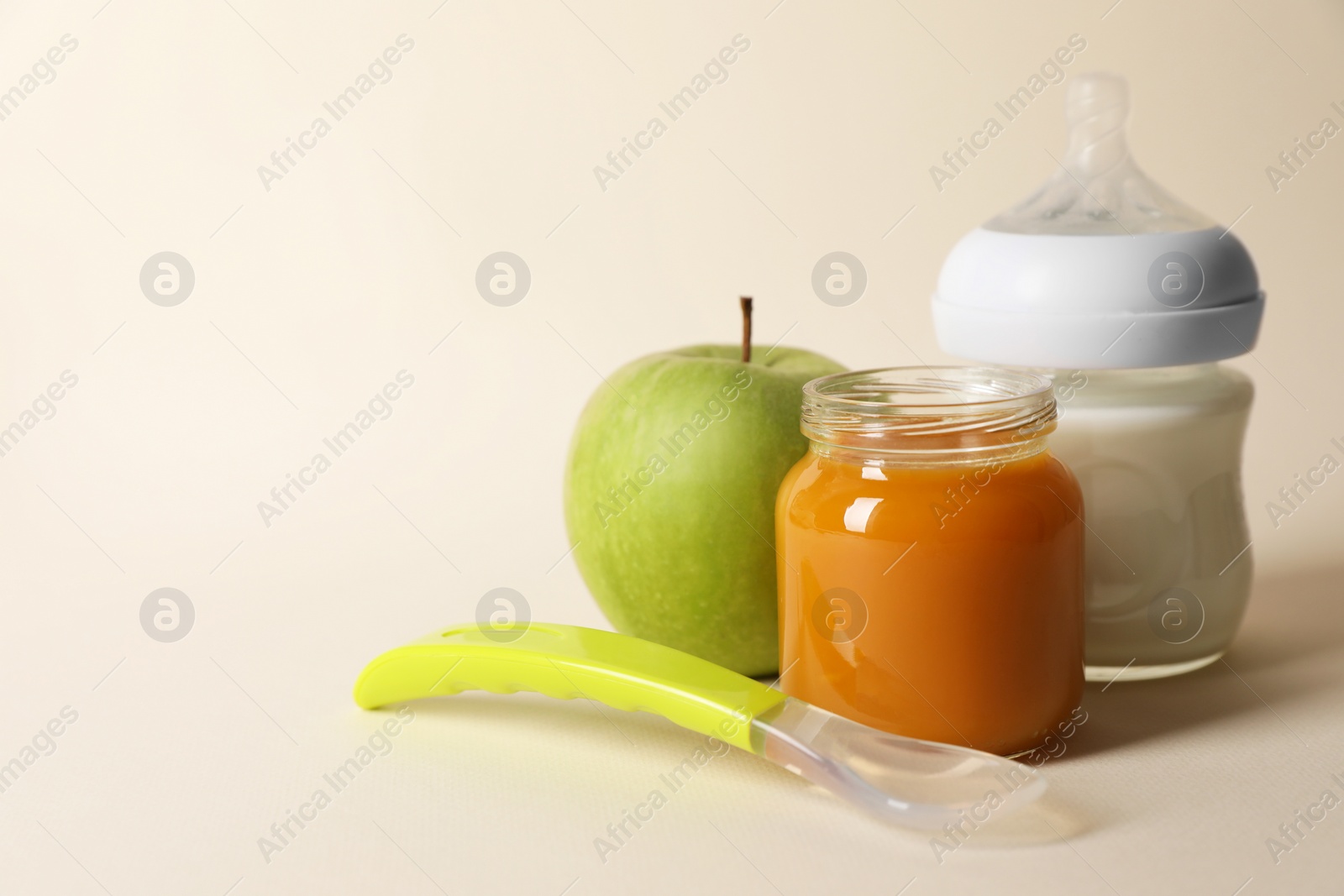 Photo of Healthy baby food in jar, bottle of milk, apple and spoon on beige background. Space for text