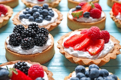 Photo of Many different berry tarts on blue wooden table. Delicious pastries