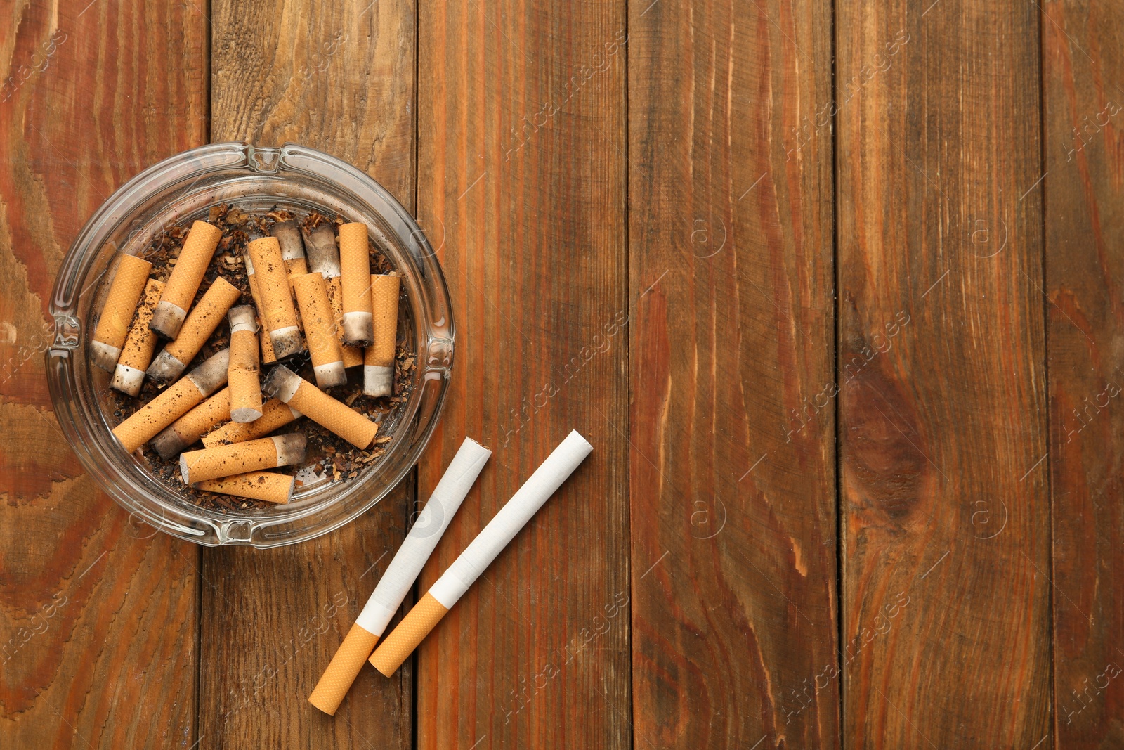 Photo of Glass ashtray with cigarette stubs on wooden table, flat lay. Space for text