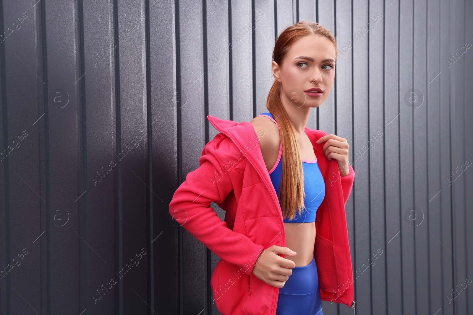 Photo of Beautiful woman in gym clothes posing near dark grey wall on street