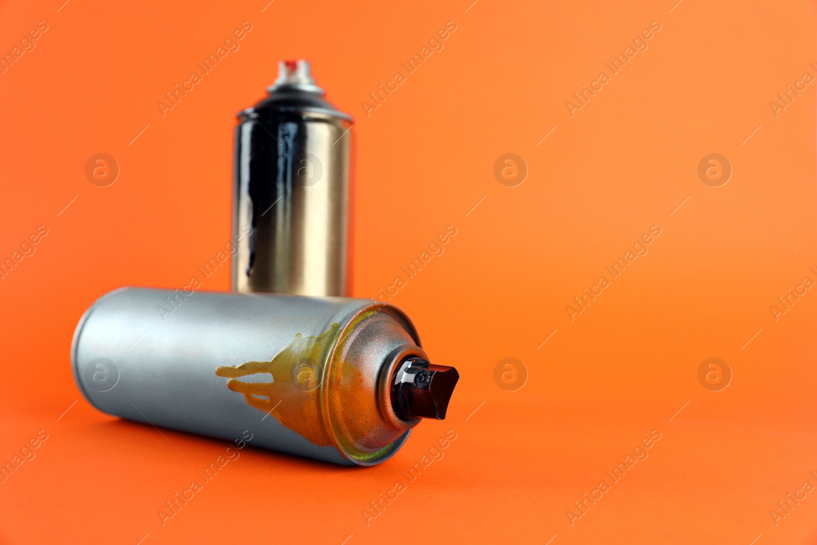 Photo of Used cans of spray paint on orange background. Space for text