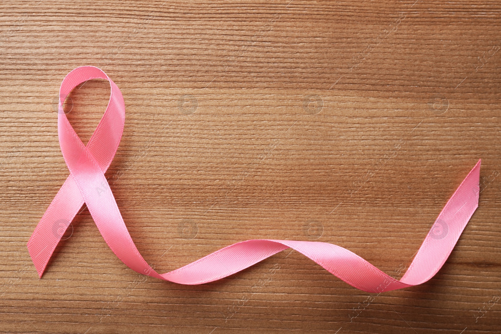 Photo of Pink ribbon on wooden background, top view with space for text. Breast cancer awareness concept