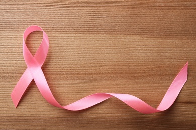 Photo of Pink ribbon on wooden background, top view with space for text. Breast cancer awareness concept