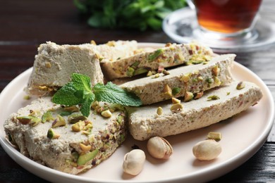 Photo of Pieces of tasty halva with pistachios and mint on table, closeup