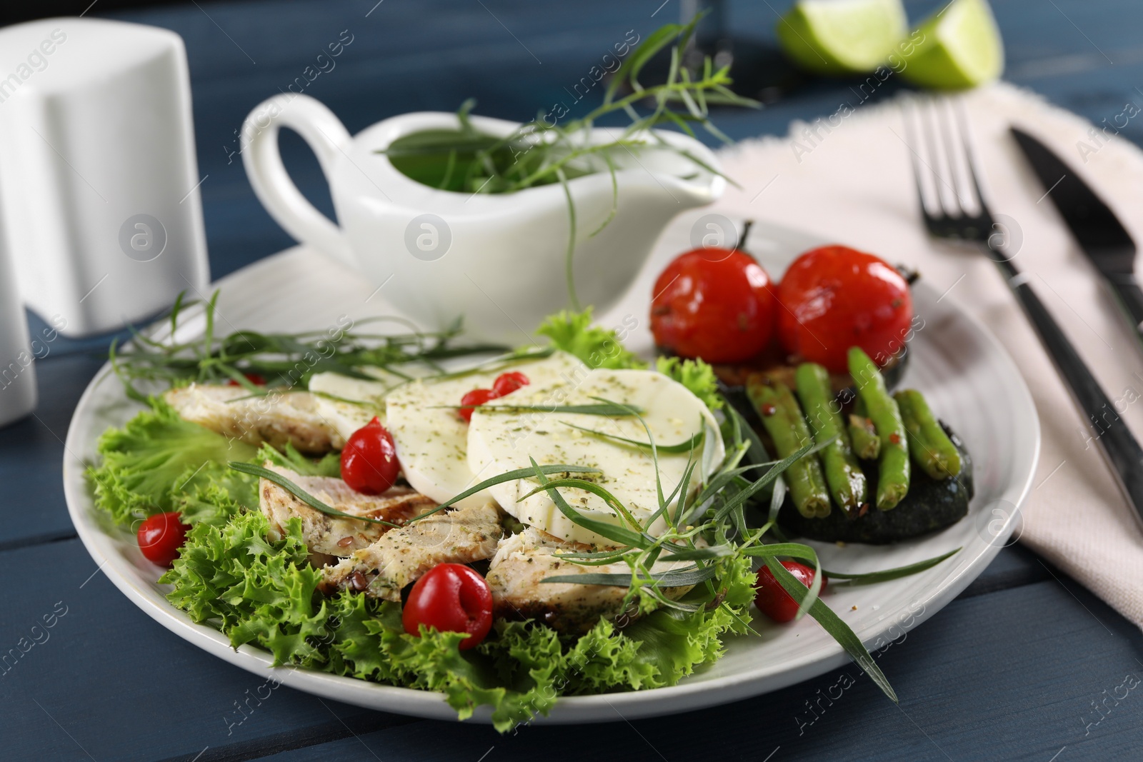 Photo of Tasty mozzarella, chicken and vegetables with tarragon served on blue wooden table, closeup