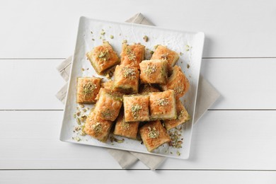 Photo of Delicious fresh baklava with chopped nuts on white wooden table, top view. Eastern sweets