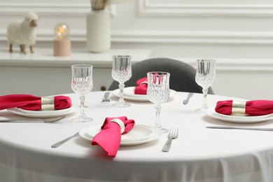 Photo of Color accent table setting. Glasses, plates, cutlery and pink napkins on table indoors