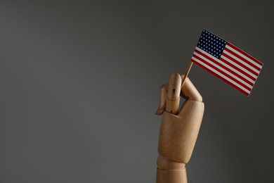 Wooden hand holding flag of USA on dark grey background, space for text