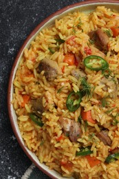 Photo of Delicious pilaf with meat on black textured table, top view