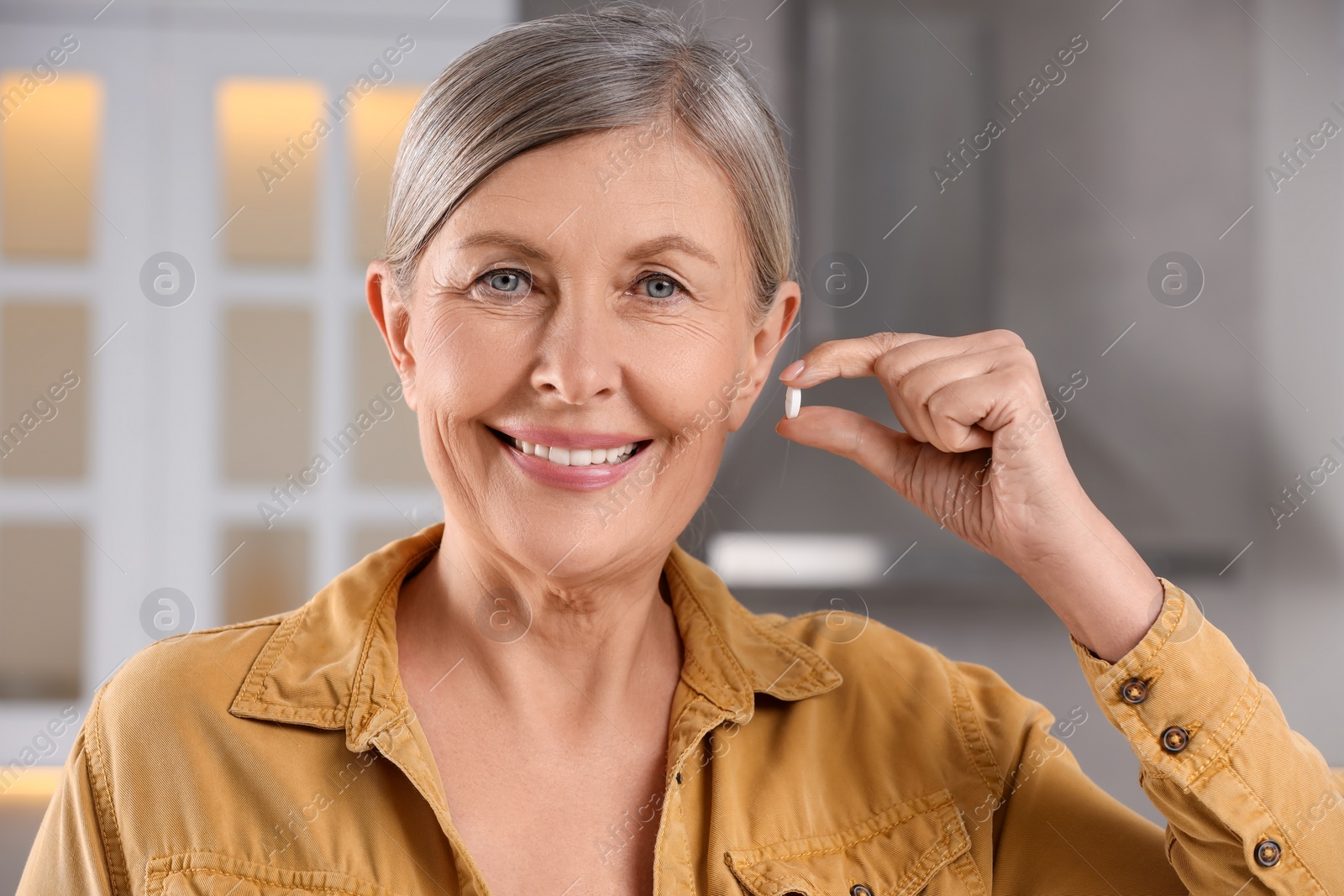 Photo of Menopause, hormone replacement therapy. Happy woman holding pill in kitchen