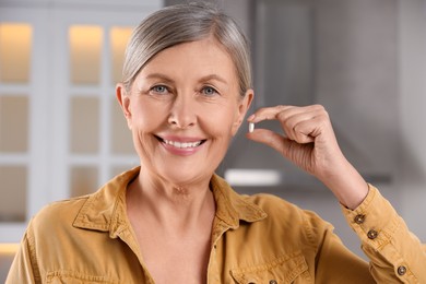 Menopause, hormone replacement therapy. Happy woman holding pill in kitchen