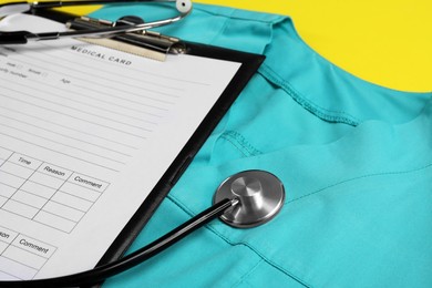 Photo of Medical uniform, stethoscope and clipboard on yellow background, closeup view